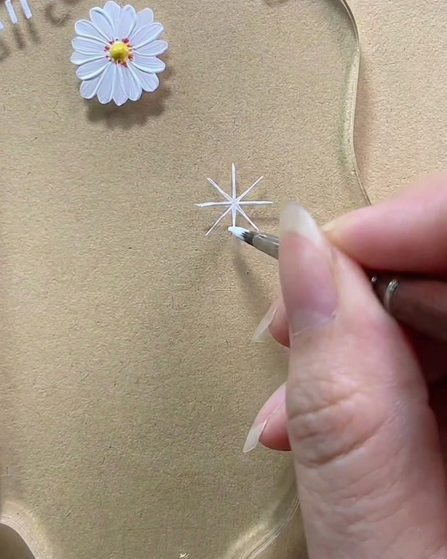 Gros plan montrant un pinceau ajoutant du gel blanc pour épaissir une ligne diagonale en un pétale en forme de goutte arrondie.