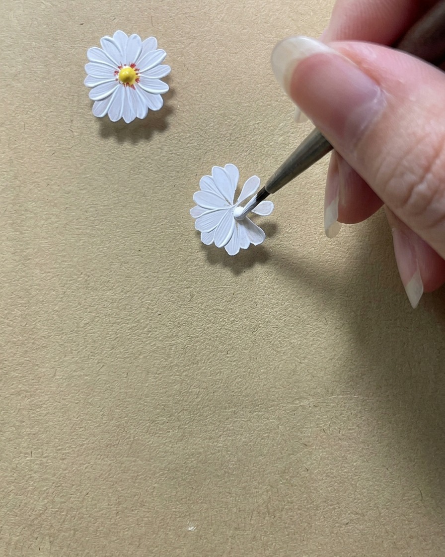 Un pinceau de précision perfectionnant les bords intérieurs des pétales de la marguerite blanche pour créer un espace circulaire au milieu.