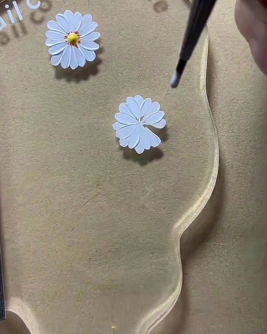 Un outil dotting plaçant un point jaune au centre dun design de marguerite blanche.