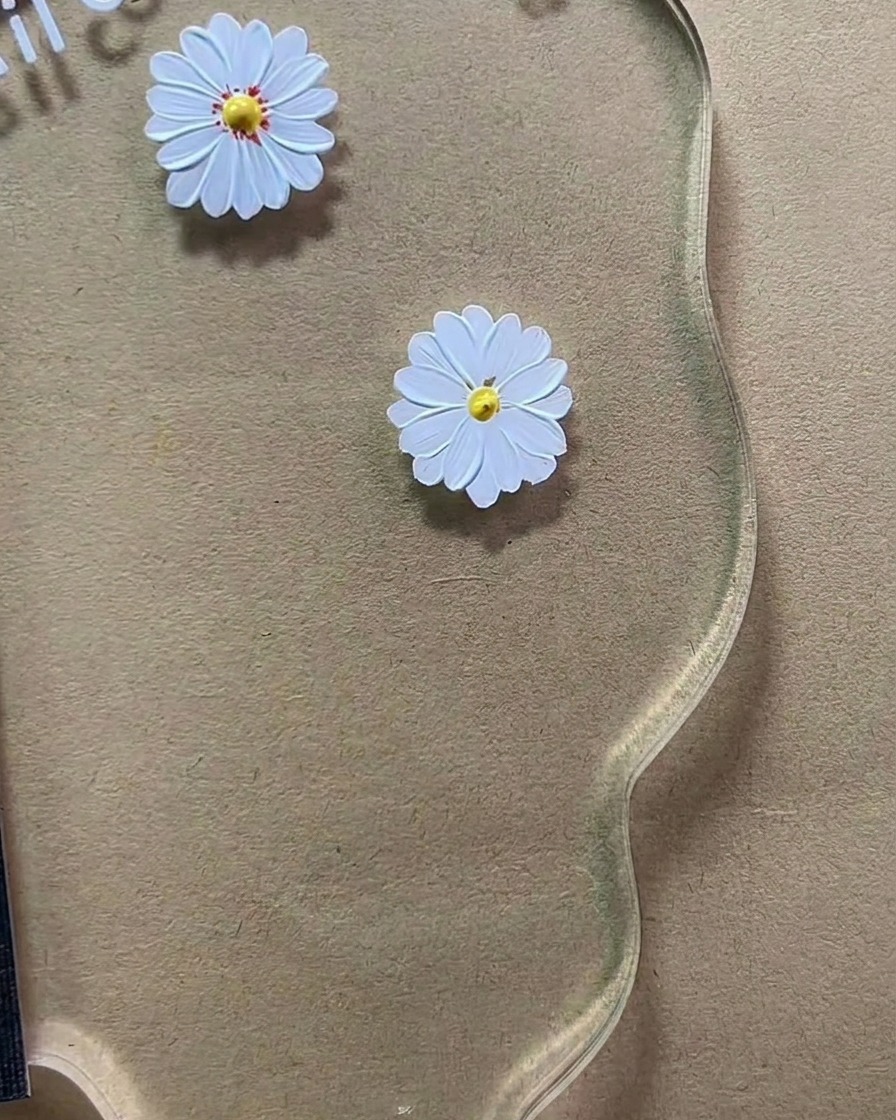 Un pinceau de précision appliquant de minuscules points brun-roux sur le centre jaune dune marguerite peinte en blanc sur une palette acrylique transparente.