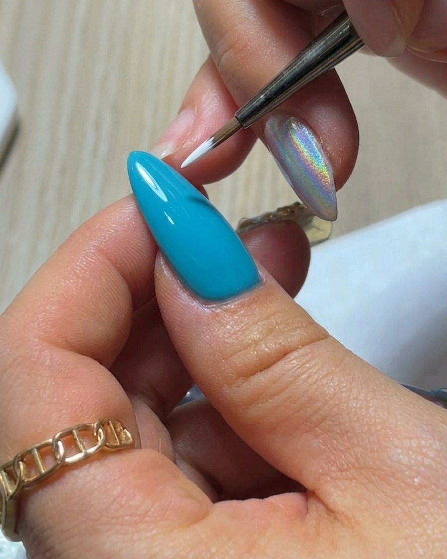 Une vue de près dun pinceau fin appliquant un pétale en gel blanc en forme de goutte sur une surface dongle bleu vif.