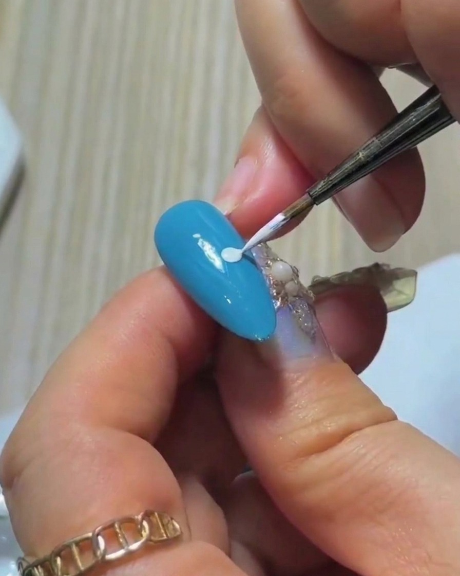 Un gros plan de la pointe dun pinceau liner fin plongé dans une petite quantité de vernis gel blanc sur une palette.