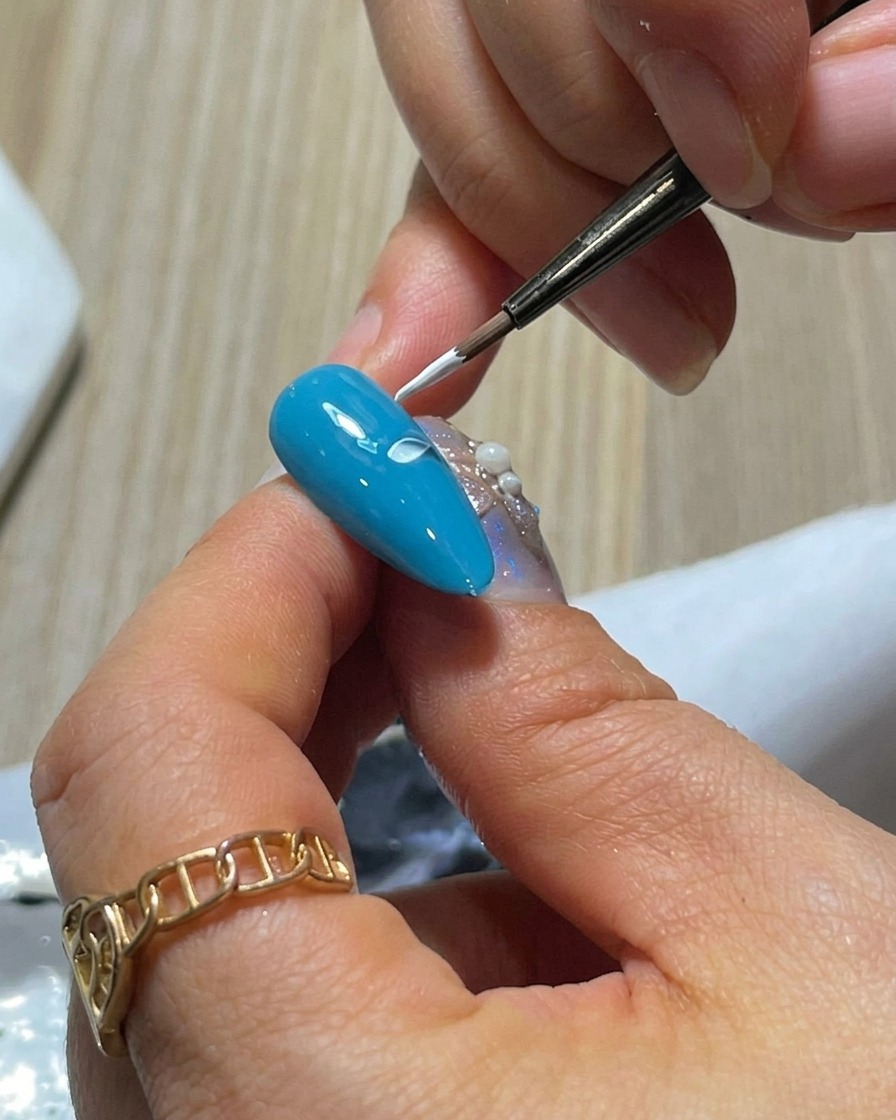 Gros plan dun ongle bleu avec deux pétales en gel blanc peints côte à côte en utilisant la technique de pression et soulèvement.