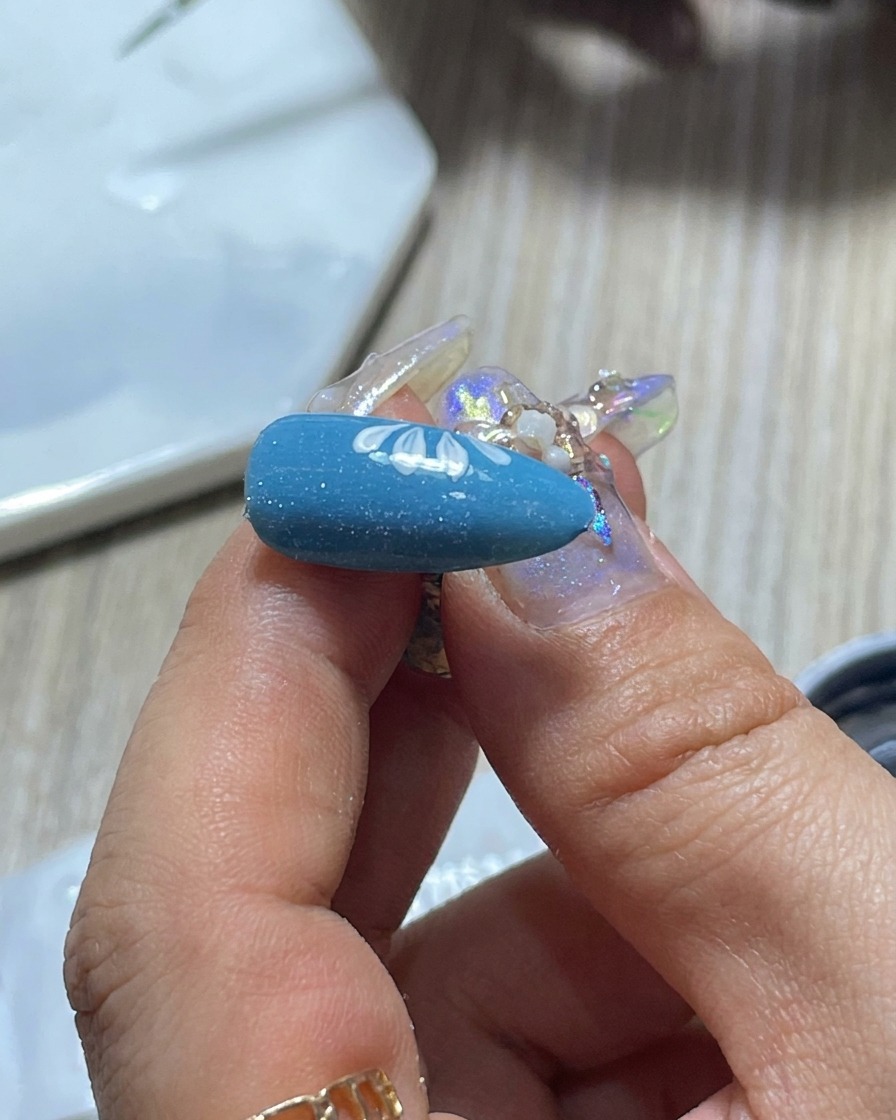 Un gros plan du pinceau dun prothésiste ongulaire essuyé sur une palette pour contrôler la quantité de vernis gel blanc.