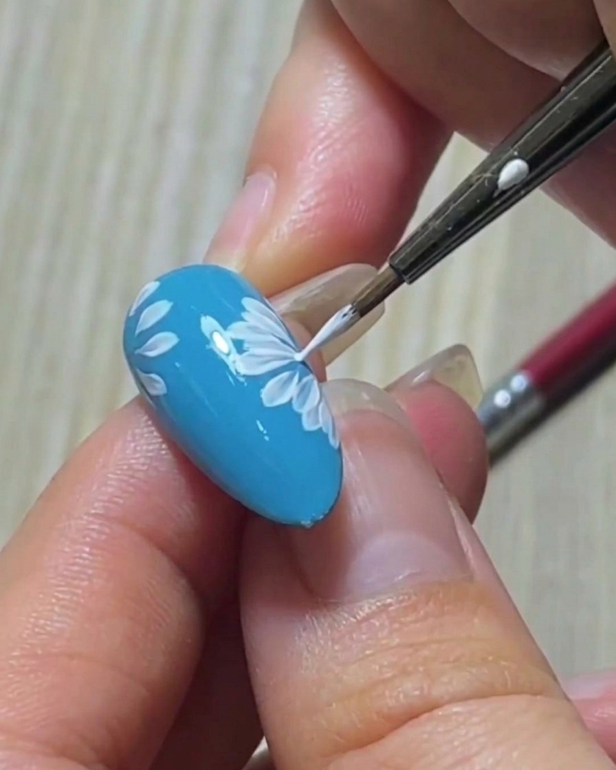 Gros plan dun pinceau liner affinant la pointe nette dun pétale blanc sur une base dongle bleu.