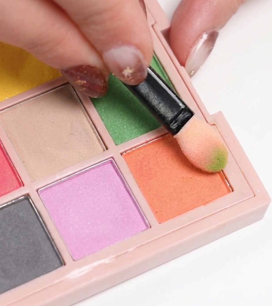 Une éponge à maquillage prélevant du vernis gel orange sur une palette pour lappliquer sur un ongle.
