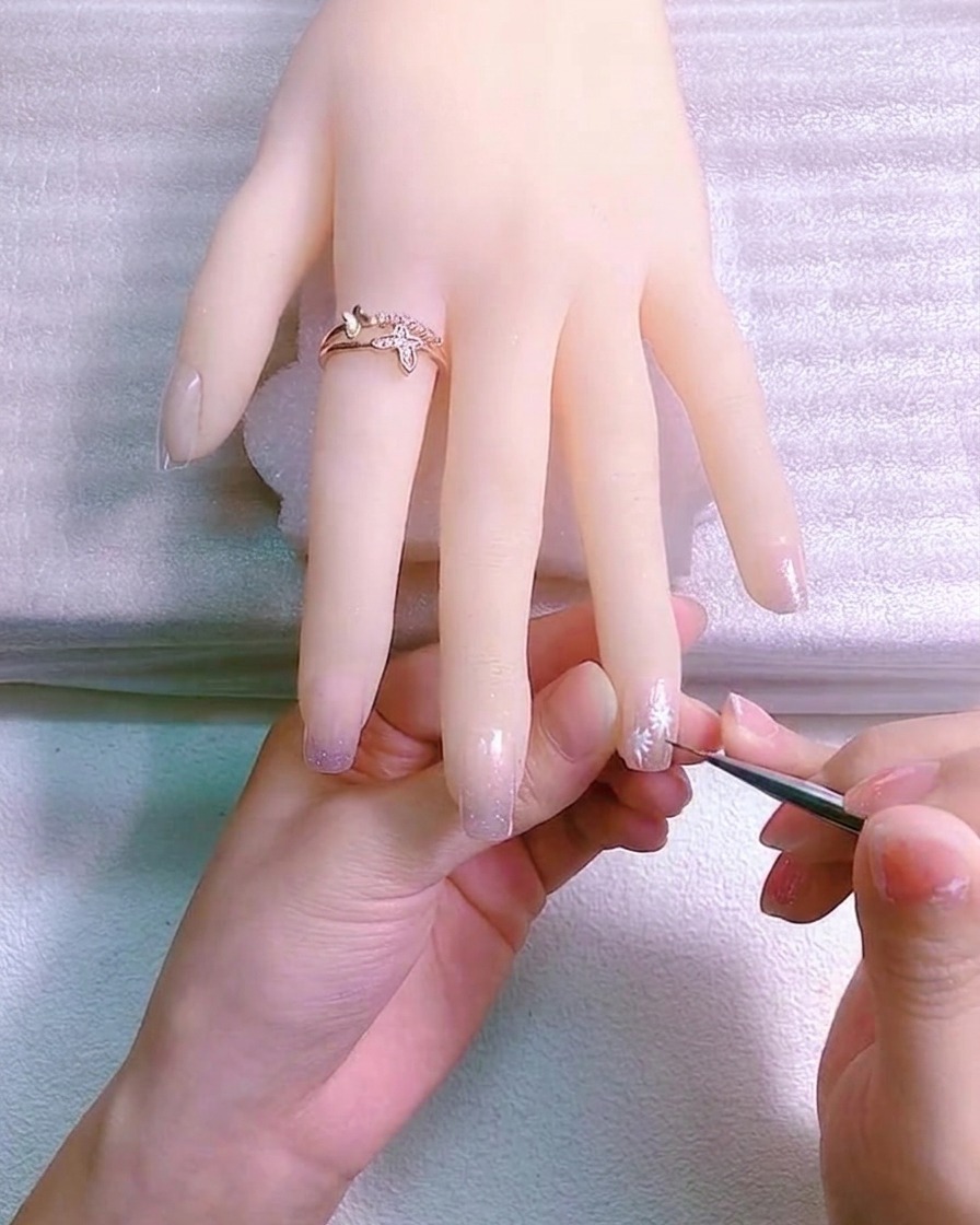 Un pinceau fin ajoutant de petits détails de feuilles vertes sur des tiges marron peintes sur un ongle.