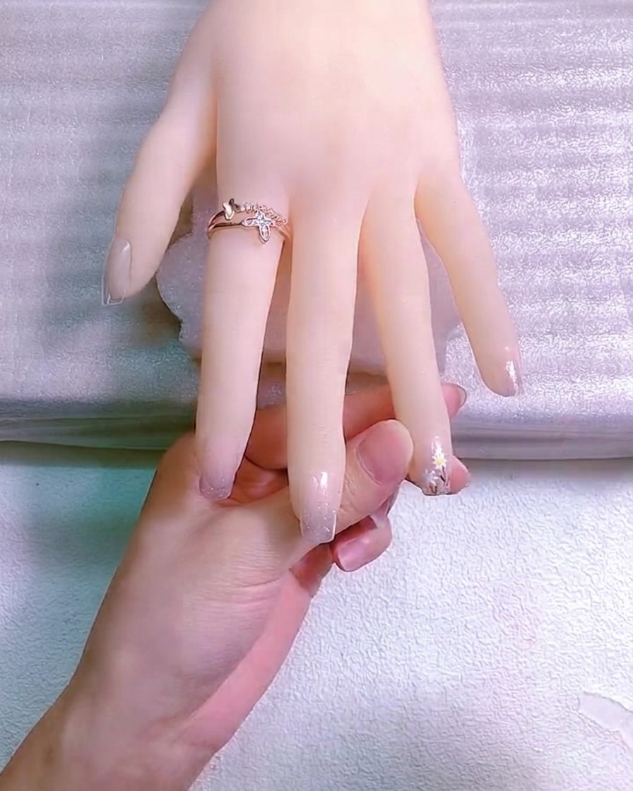 Gros plan dun outil de dotting appliquant un centre en gel jaune sur une petite marguerite blanche peinte à la main sur un ongle.