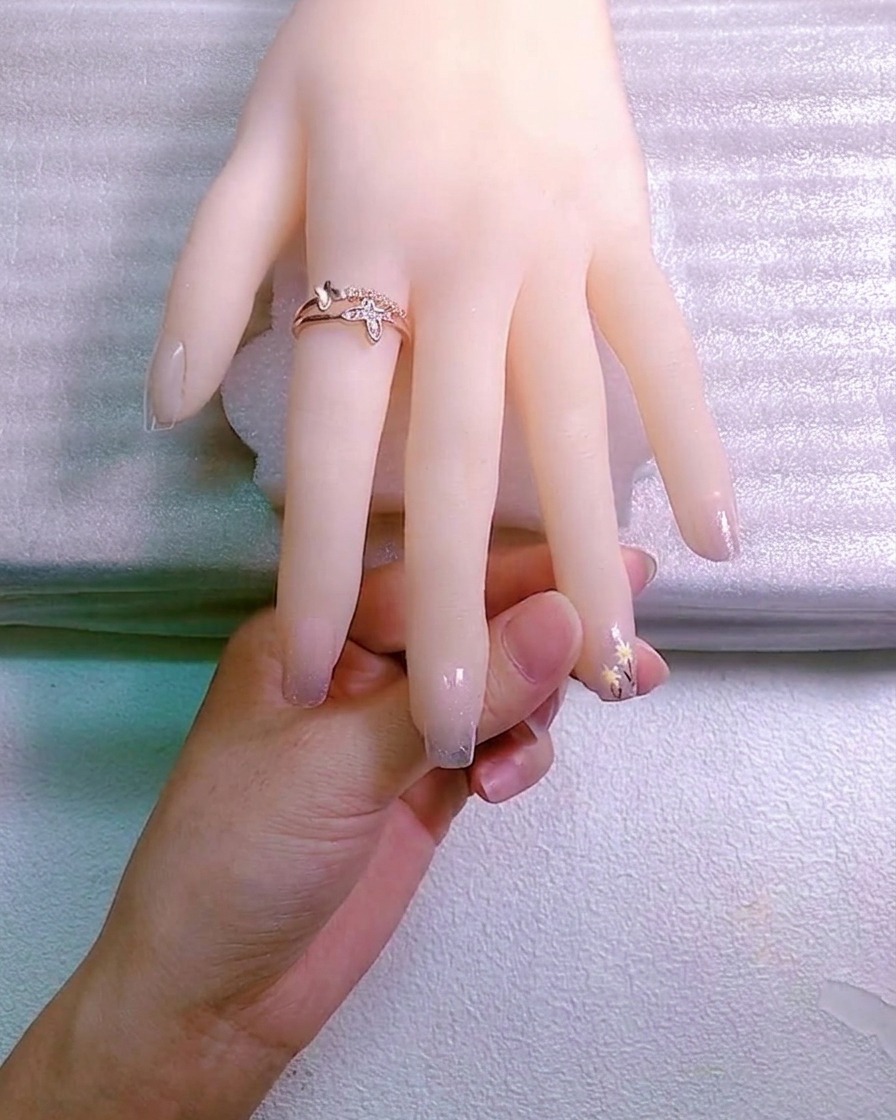 Une prothésiste ongulaire utilisant un outil pour placer un petit charme en cristal dans une goutte de gel adhésif sur un ongle.