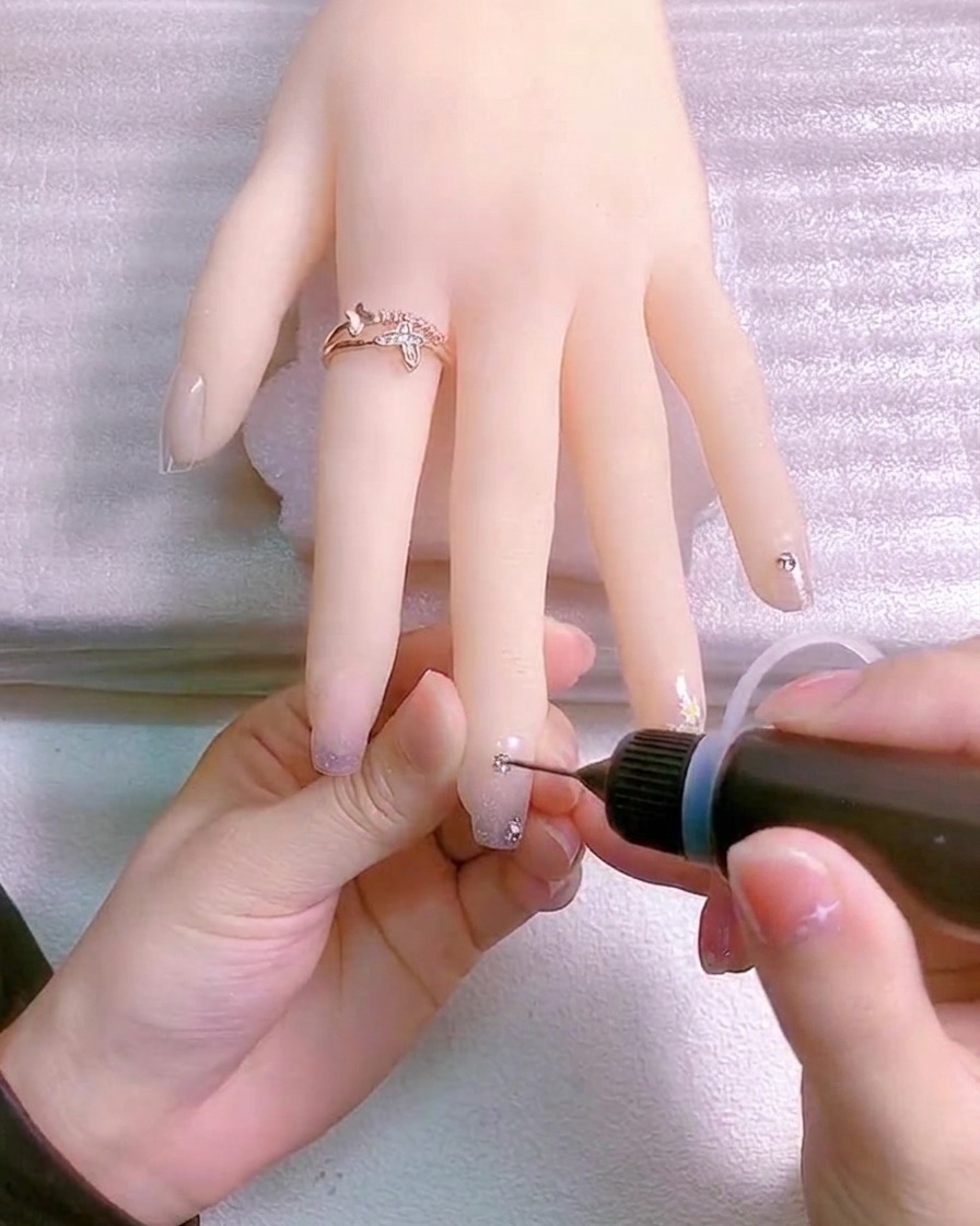 Un pinceau fin appliquant du gel transparent autour de la base dun charme en cristal sur un ongle pour le sécuriser.