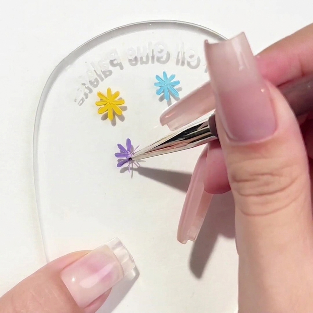 Un pinceau liner appliquant un troisième pétale violet sur le motif de marguerite.