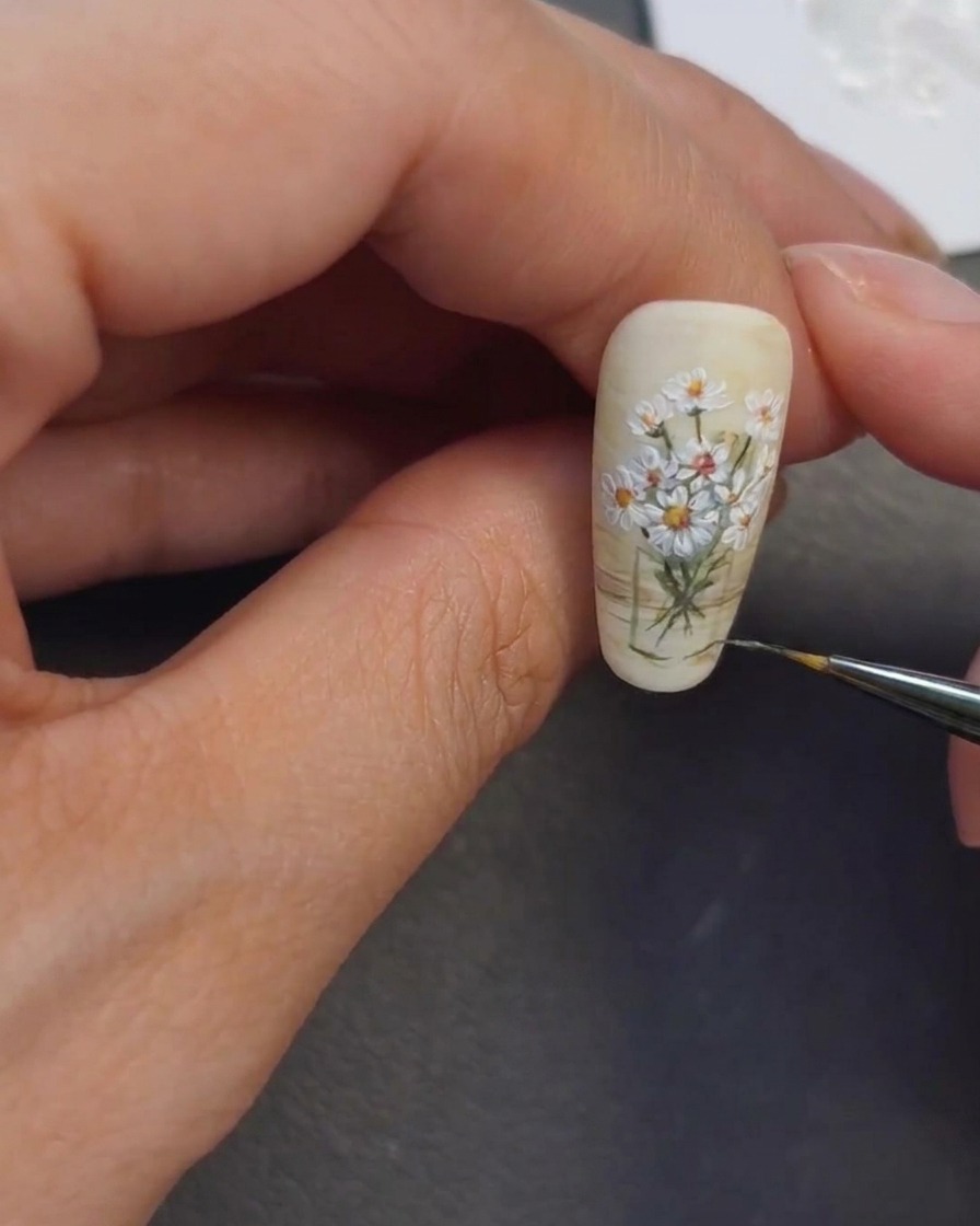 Une styliste ongulaire appliquant des reflets clairs sur la zone du vase.