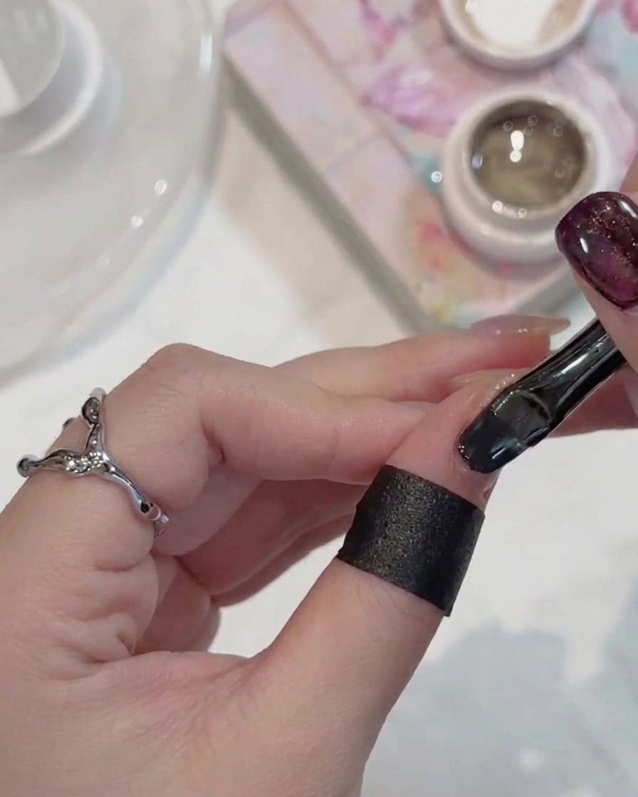 Un pinceau à ongles appliquant un vernis gel cat-eye sombre et scintillant sur un ongle.