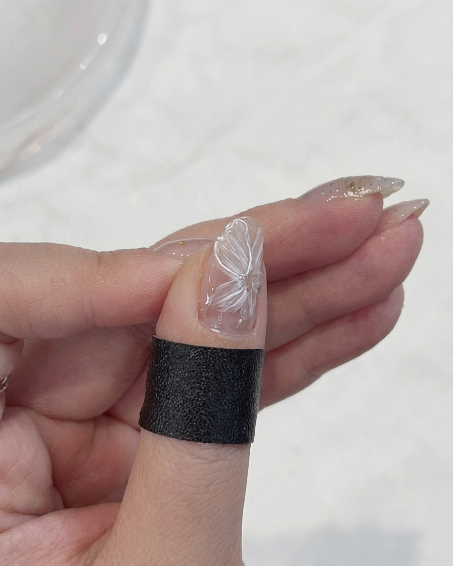 Un pinceau liner fin traçant les bords délicats des pétales de fleur blancs sur un ongle.