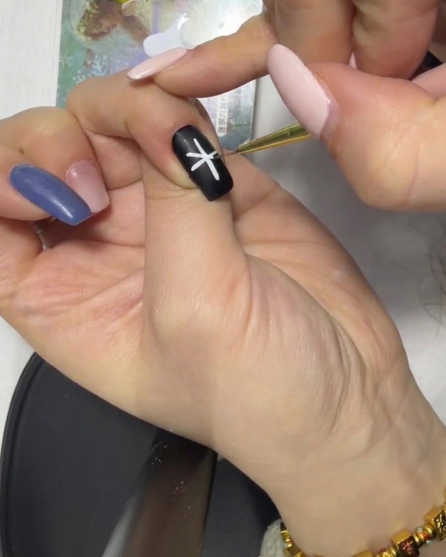 Gros plan dune forme dastérisque blanche complétée au centre dun ongle noir.