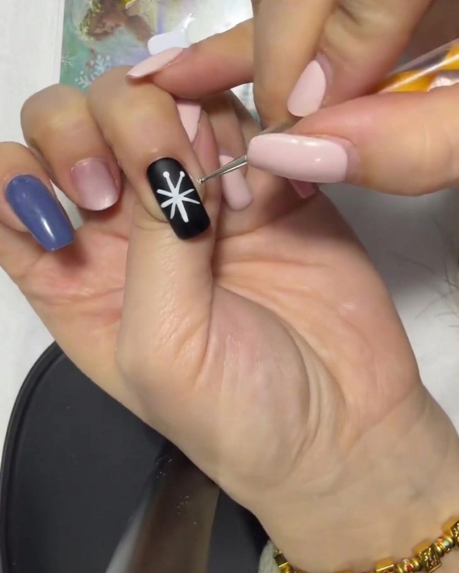 Gros plan dun ongle noir avec une étoile blanche dont les pointes sont reliées au centre par un pinceau.