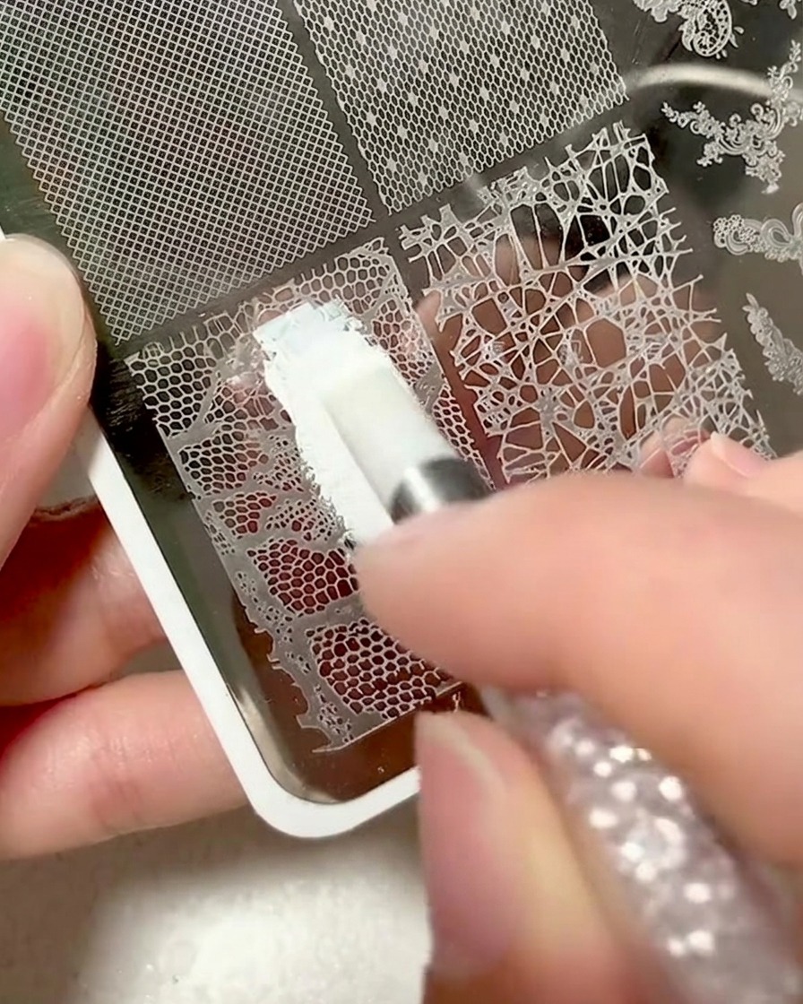 Gros plan dune plaque métallique avec un motif de dentelle recouvert de gel destampage blanc.