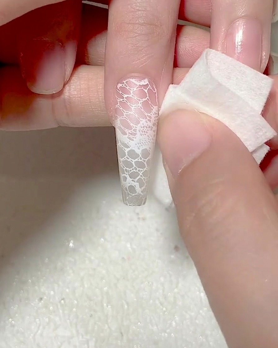 Une éponge utilisée pour nettoyer les bords dun design de dentelle sur un ongle.
