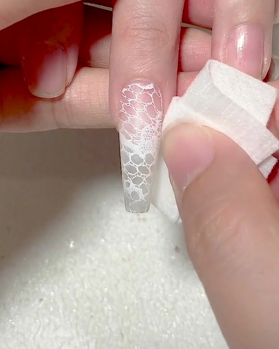 Gros plan dune éponge de maquillage tamponnant du gel blanc sur le bout dun ongle pour un effet ombré.
