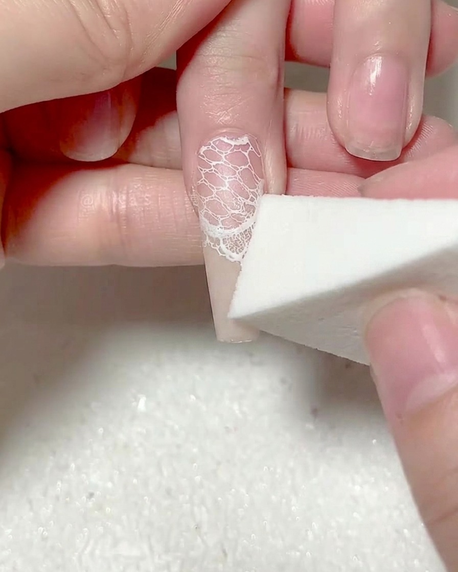 Une éponge de maquillage appliquant une deuxième couche de gel blanc sur le bout de longle.