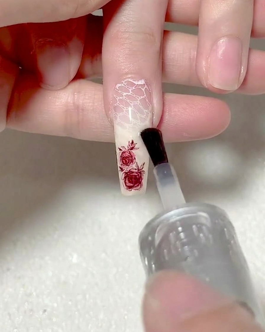 Un pinceau appliquant du gel de base transparent sur un autocollant rose pour lencapsuler.