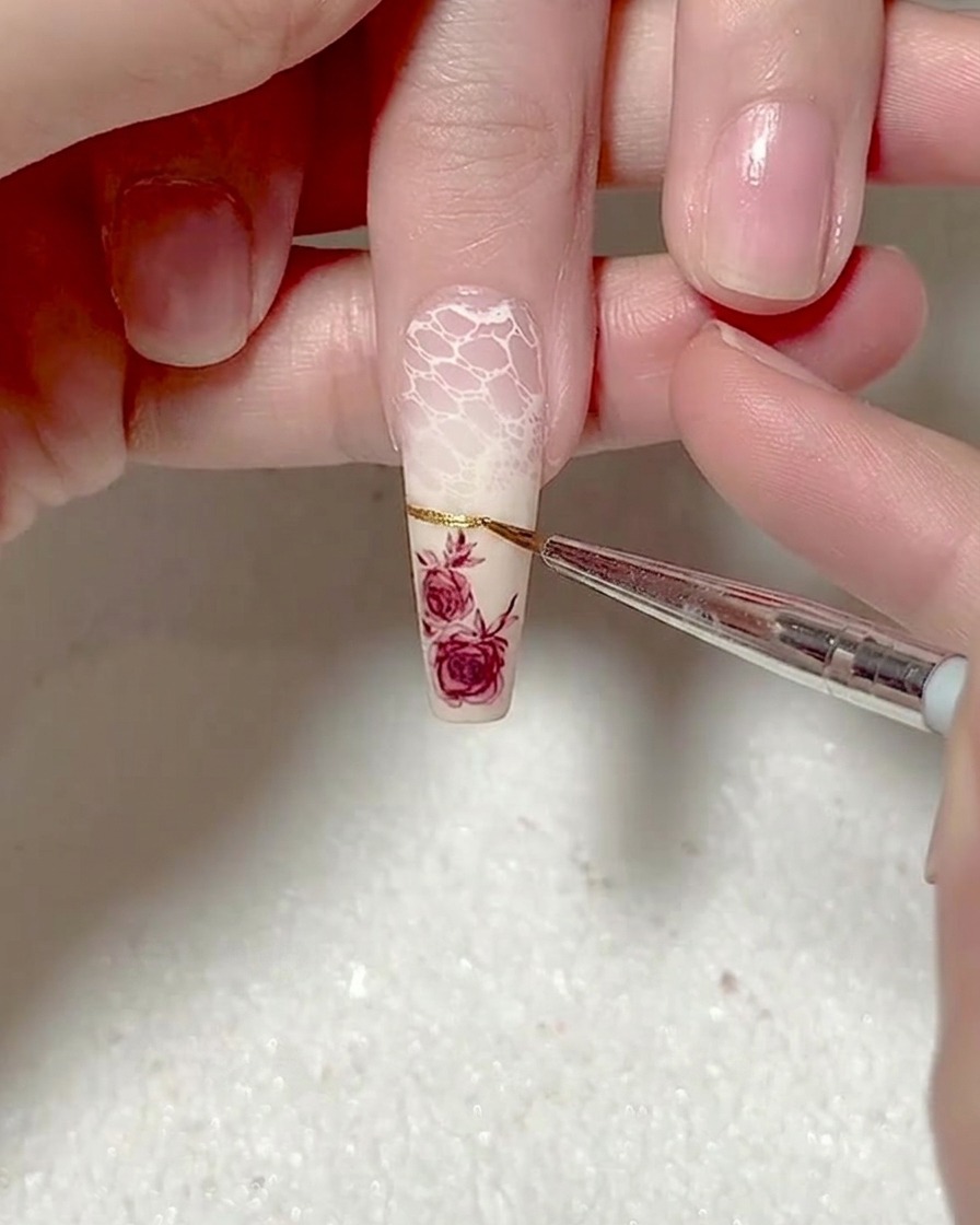 Gros plan dun pinceau liner appliquant une ligne fine de gel doré métallisé pour une french manucure.
