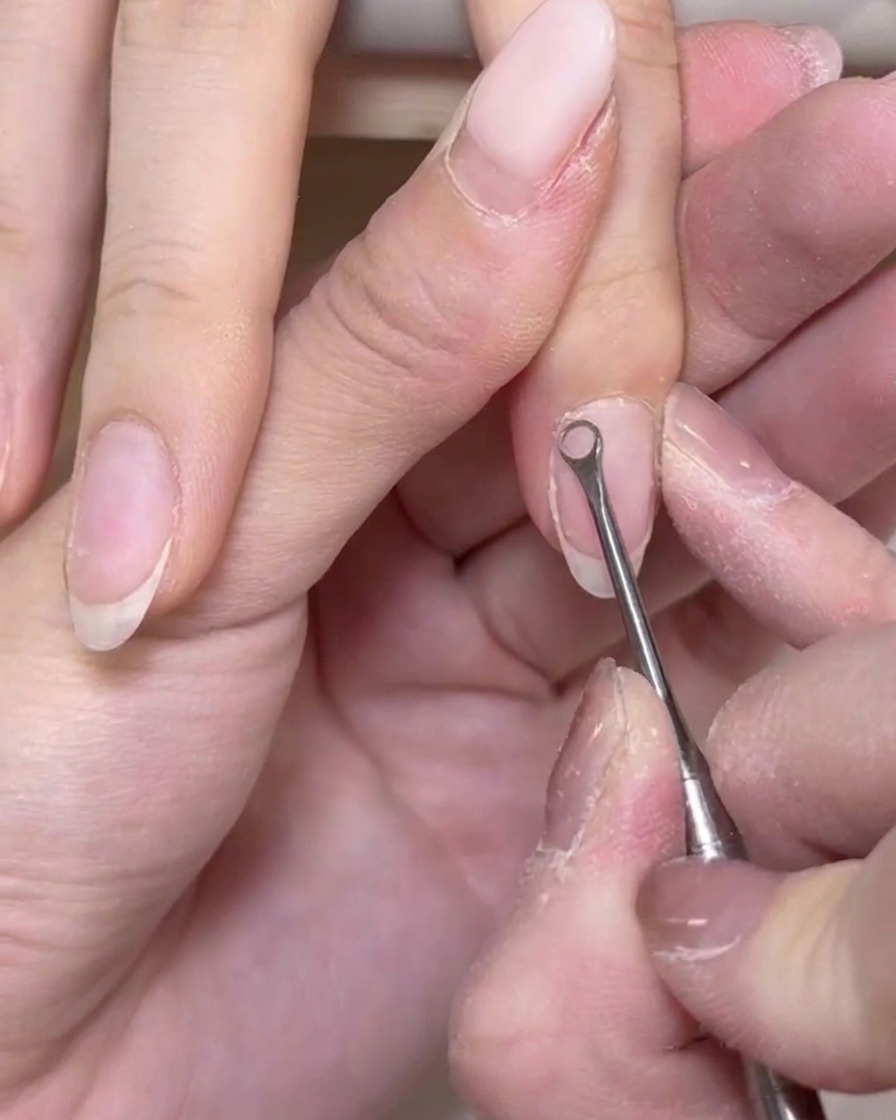 Un plan rapproché dun repousse-chair en métal grattant doucement les cellules mortes à la surface dun ongle naturel.