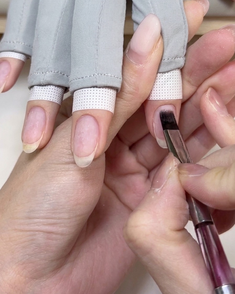 Un pinceau plat pour gel appliquant une base transparente sur un ongle naturel.