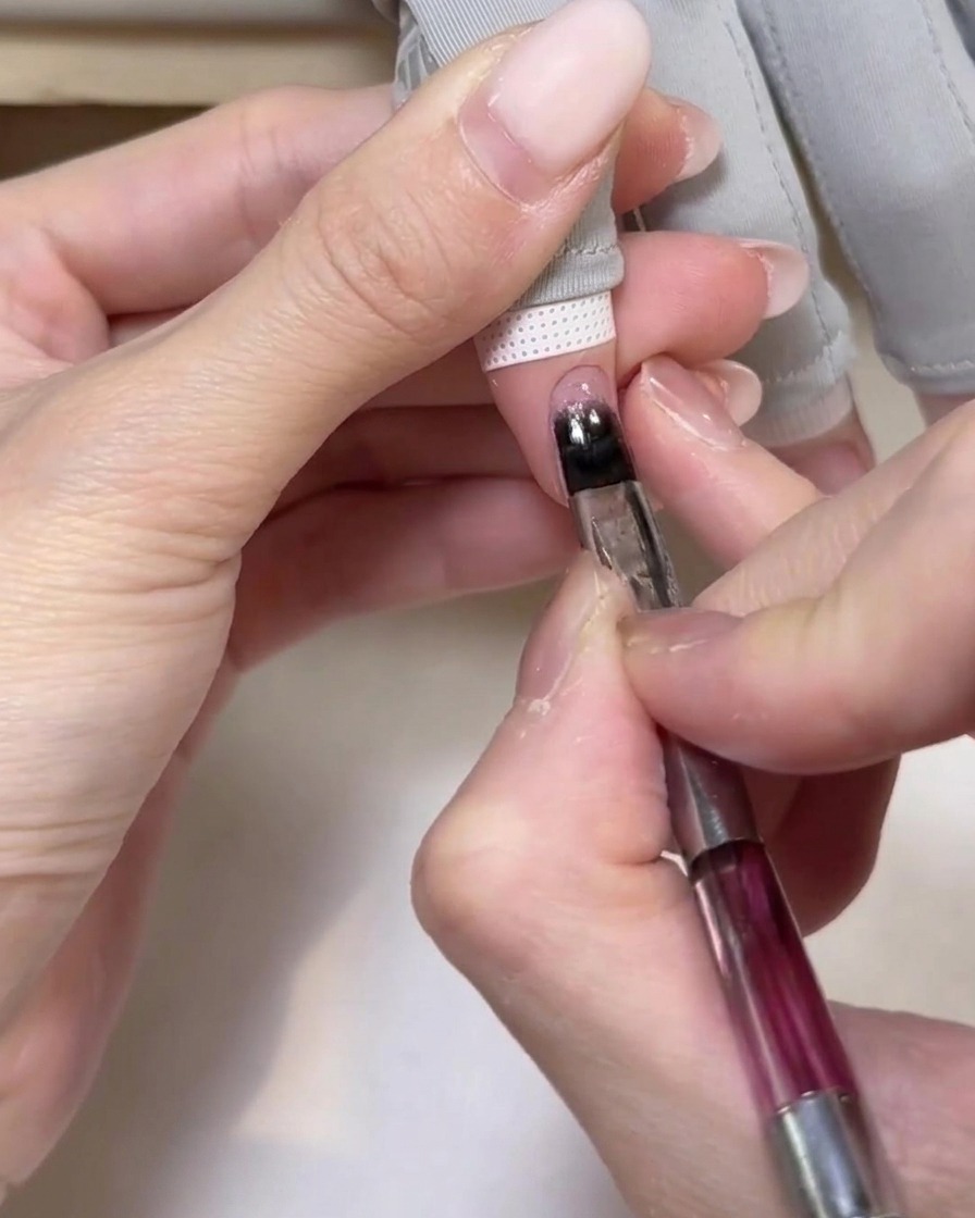 Une main positionnée sous une lampe UV portable, les ongles recevant la lumière pour catalyser le gel.