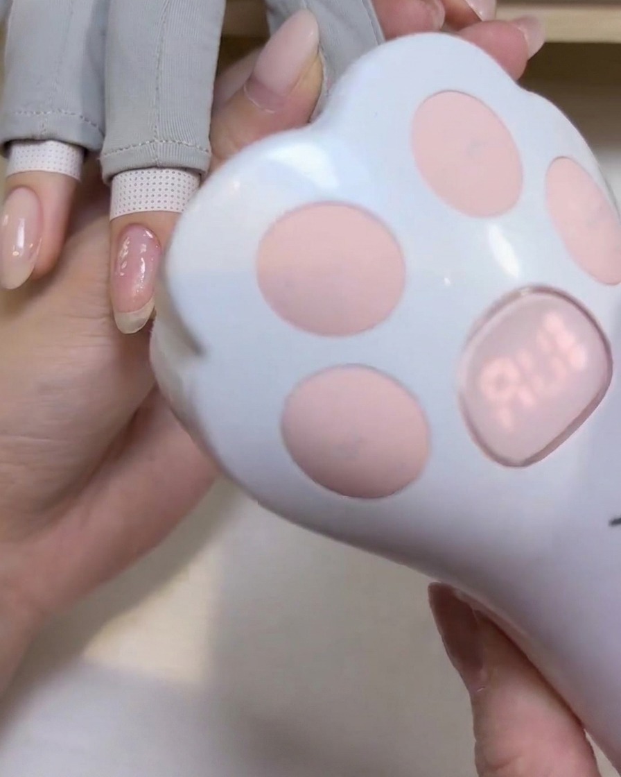 Une jolie lampe UV/LED portative en forme de patte de chat positionnée au-dessus dun doigt pour catalyser le gel.