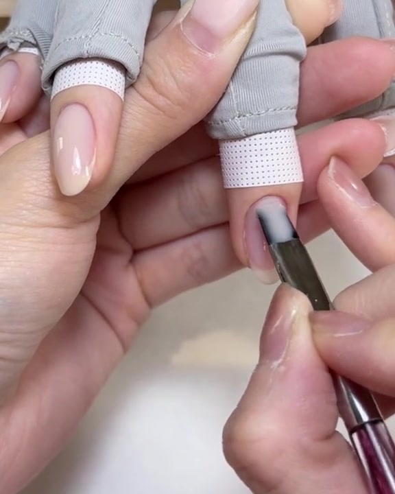 Un pinceau plat appliquant une couche lisse de gel de transfert transparent sur un ongle en gel rose.