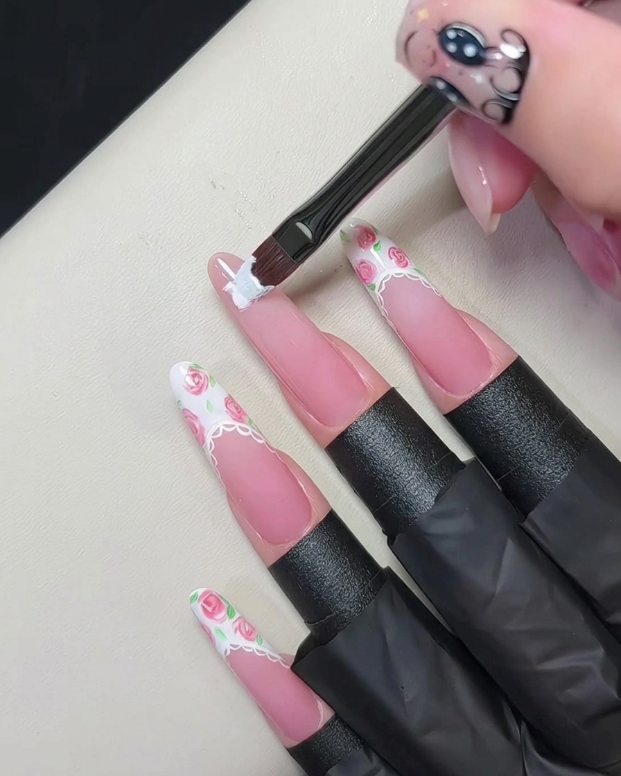 Un pinceau plat à gel appliquant une French blanche épaisse sur le bord dun ongle rose nude.
