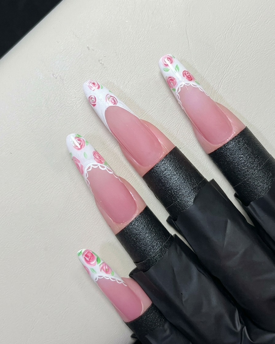 Un pinceau liner fin peignant de minuscules feuilles autour des roses sur une French blanche.