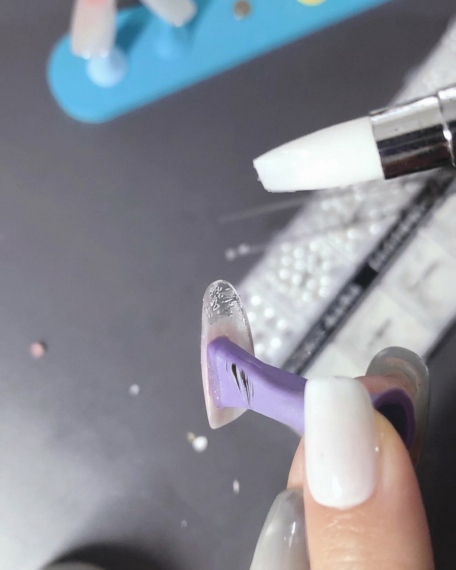 Un pinceau appliquant une petite goutte de gel transparent sur la surface de longle durci.