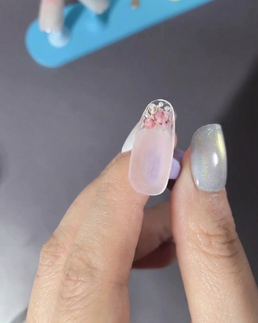 Un pinceau appliquant un top coat transparent sur un ongle décoré.