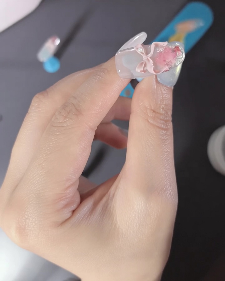Gros plan dun doigt avec un nœud 3D rose et des perles sur longle.