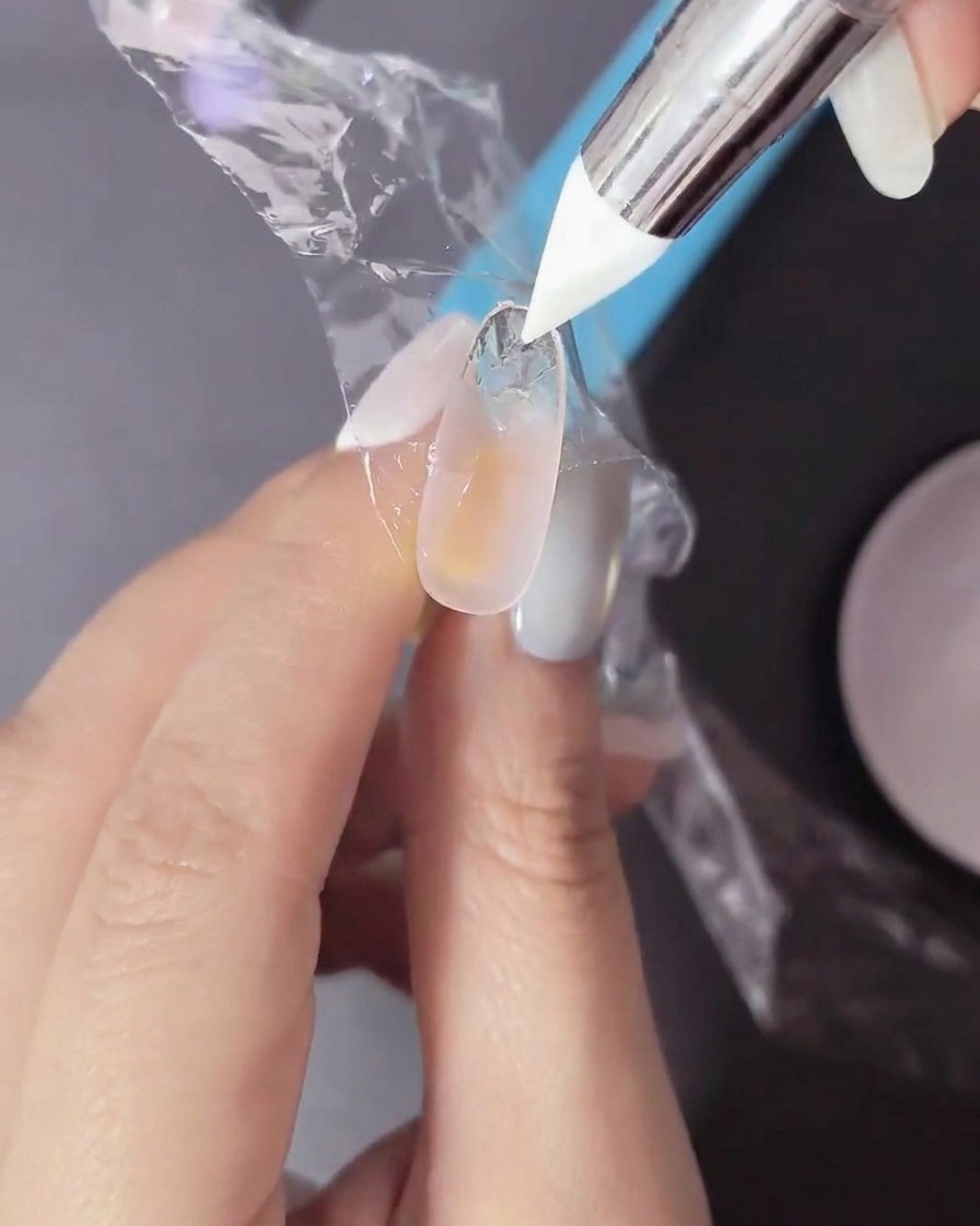 Un ongle avec du gel non catalysé recouvert dun film plastique pressé par un outil en silicone.