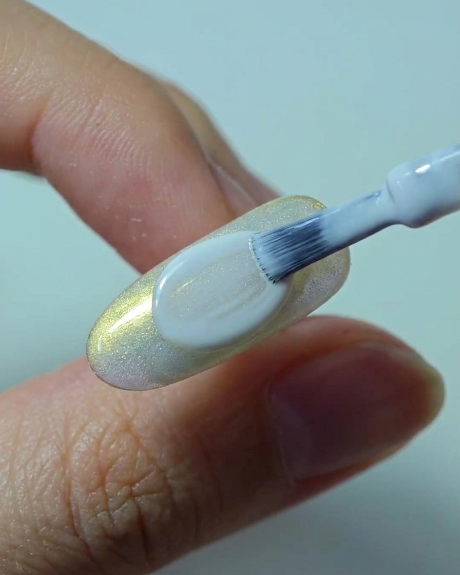 Un pinceau appliquant une seconde couche opaque et lisse de vernis gel blanc sur longle.