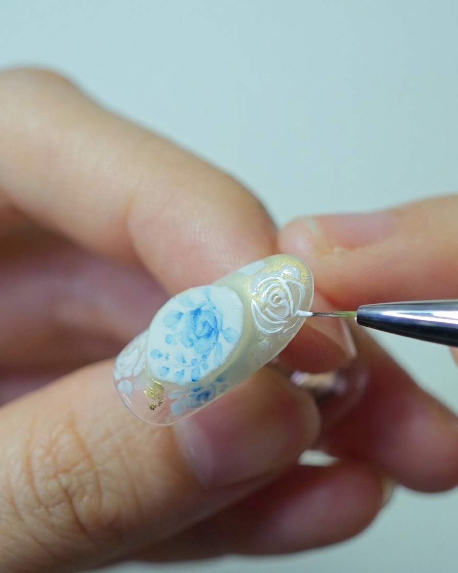 Gros plan dun pinceau appliquant du gel relief blanc épais sur les contours de rose précédemment peints pour créer du relief.