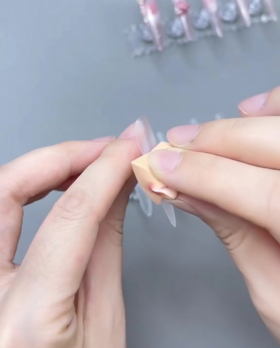 Un pinceau estompant le gel rose sur la capsule pour créer un dégradé ombré.