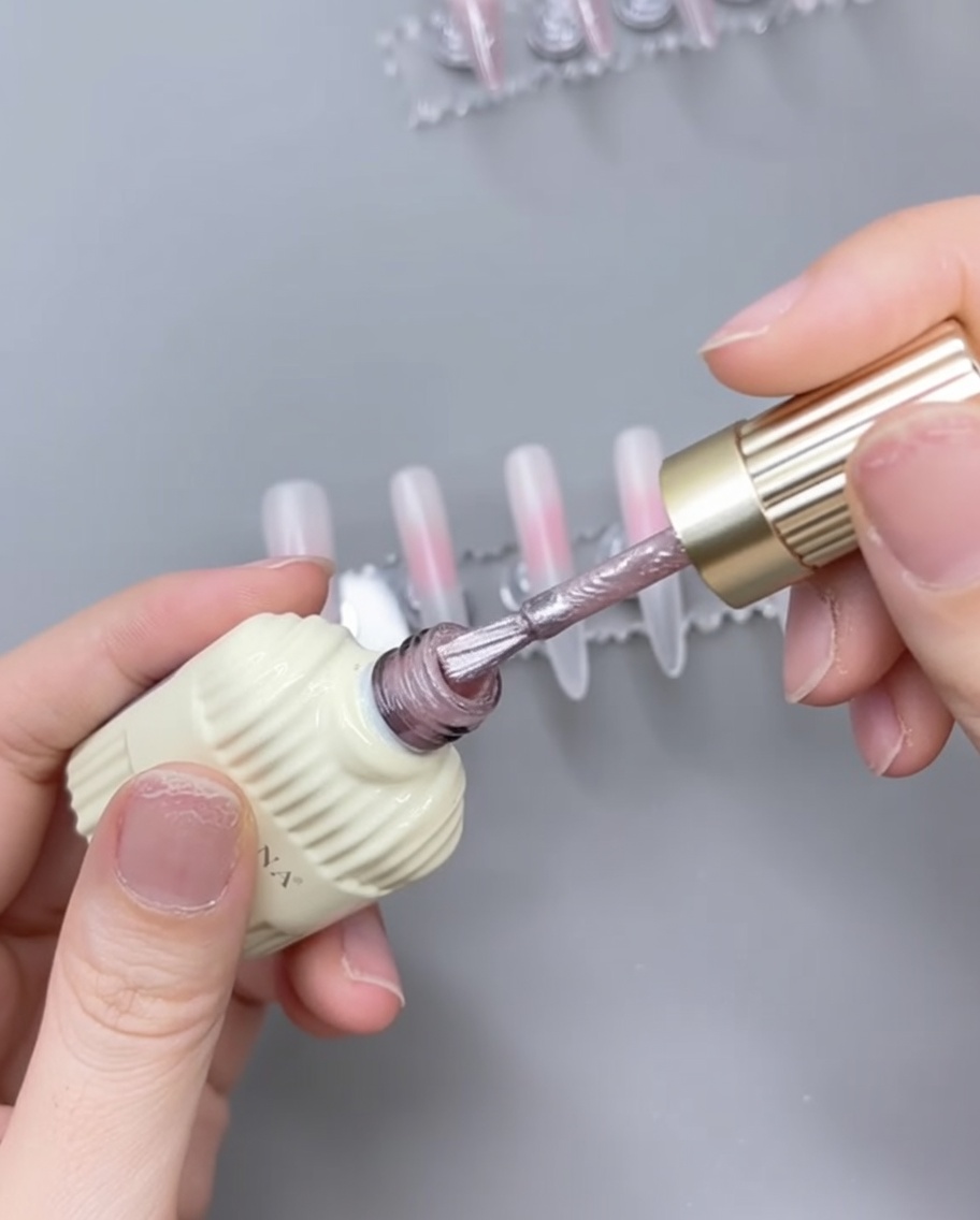Un pinceau appliquant du gel œil-de-chat rose sur une base rose translucide catalysée.