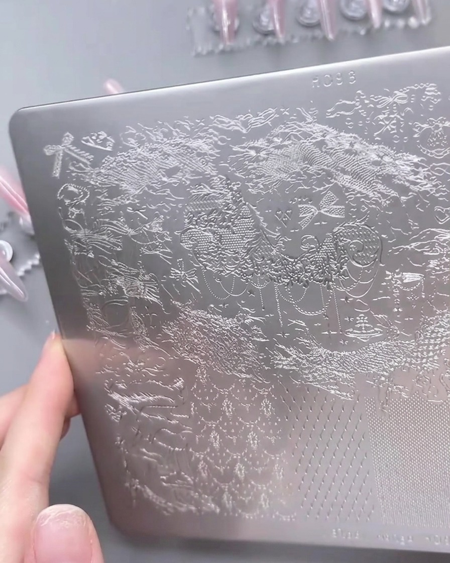 Gros plan sur une plaque de stamping avec du vernis blanc étalé sur un motif de dentelle détaillé.