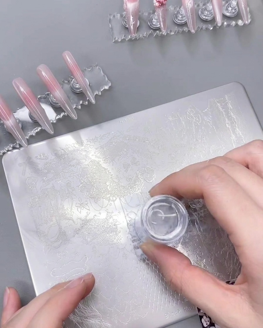 Un tampon en silicone transparent pressé sur une plaque de stamping, soulevant le motif en dentelle blanche.