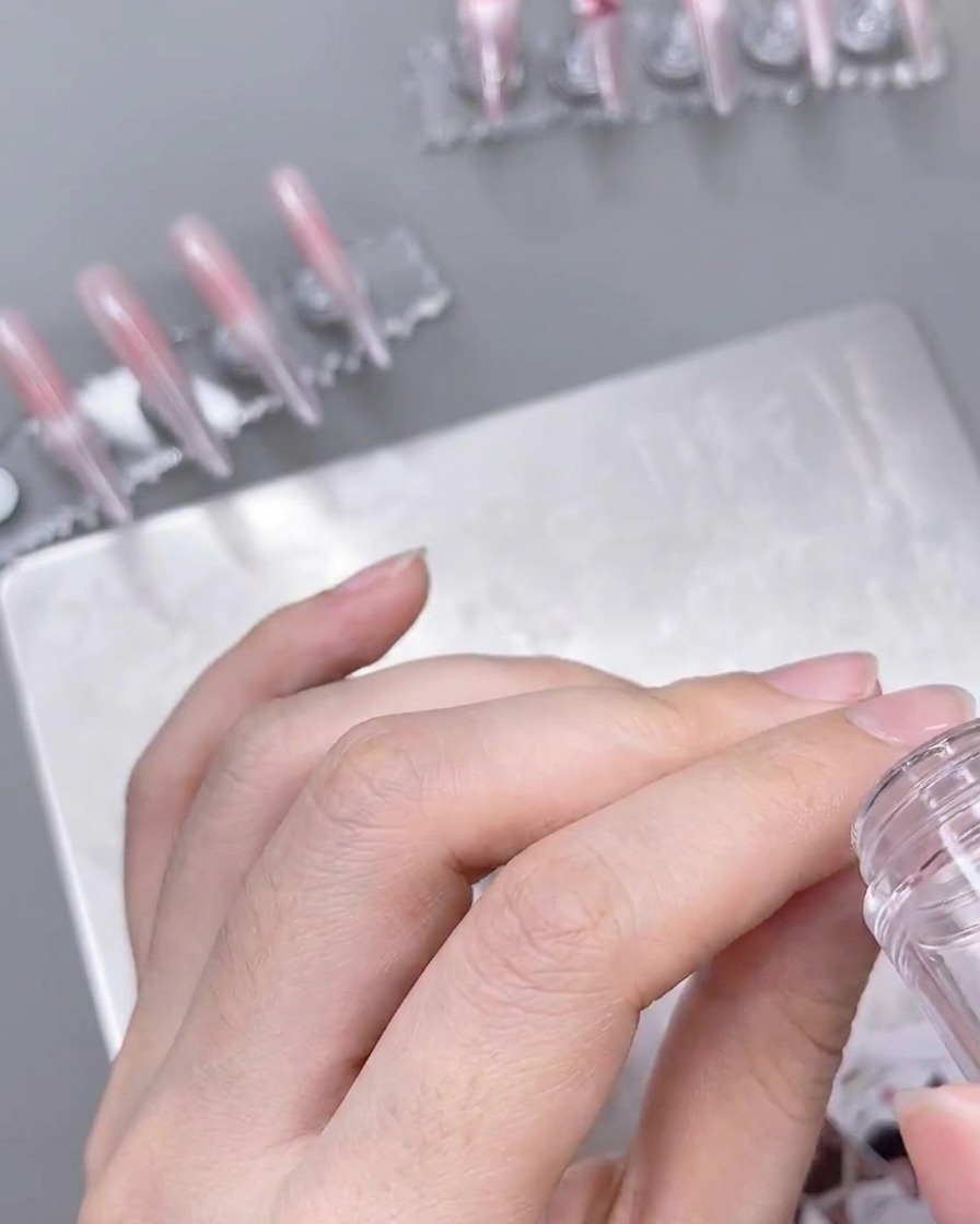 Un tampon transparent appliquant un motif de dentelle blanche sur un ongle ombré préparé.