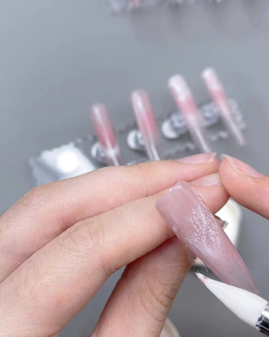 Un pinceau liner fin créant des lignes roses précises sur un ongle décoré.