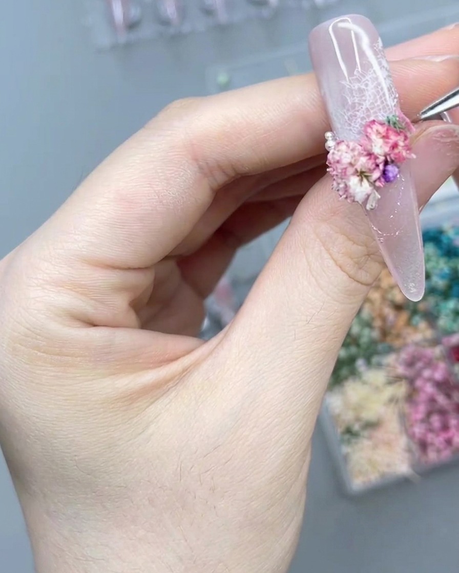 Gros plan sur lutilisation dun outil de précision pour placer une petite perle près dun groupe de fleurs roses.