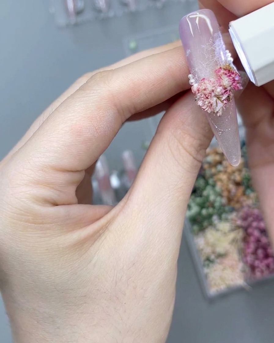 Une lampe UV/LED portable éclairant une composition florale 3D sur un ongle.
