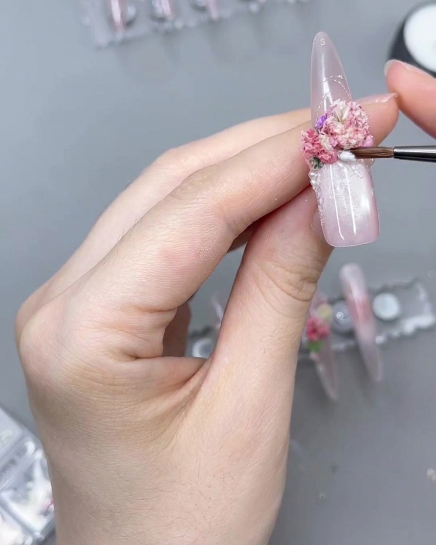 Gros plan sur un pinceau de précision appliquant du gel transparent autour dune composition florale.