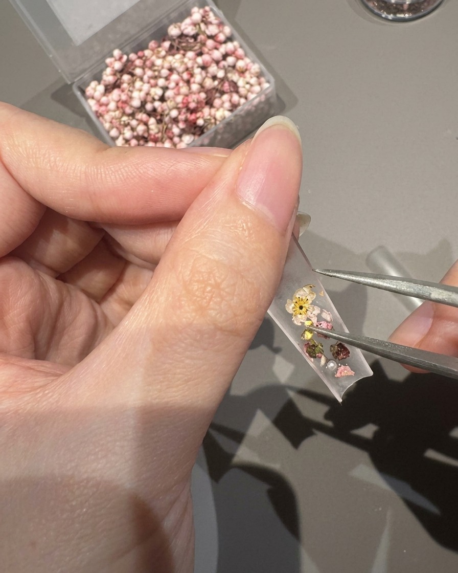 Gros plan sur une pince déposant des perles minuscules et des cristaux sur une capsule décorée de fleurs.