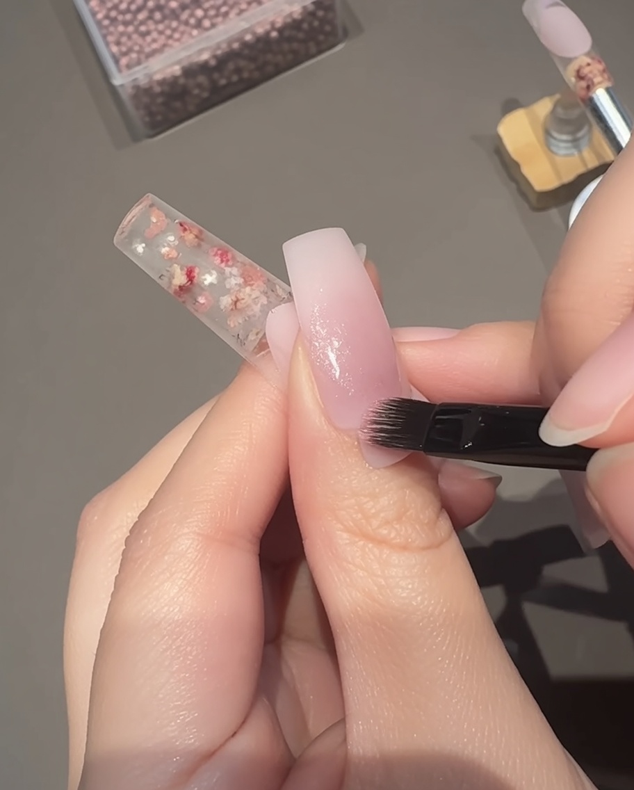 Application dun gel cat-eye magnétique rose transparent sur la plaque de longle avec un pinceau.